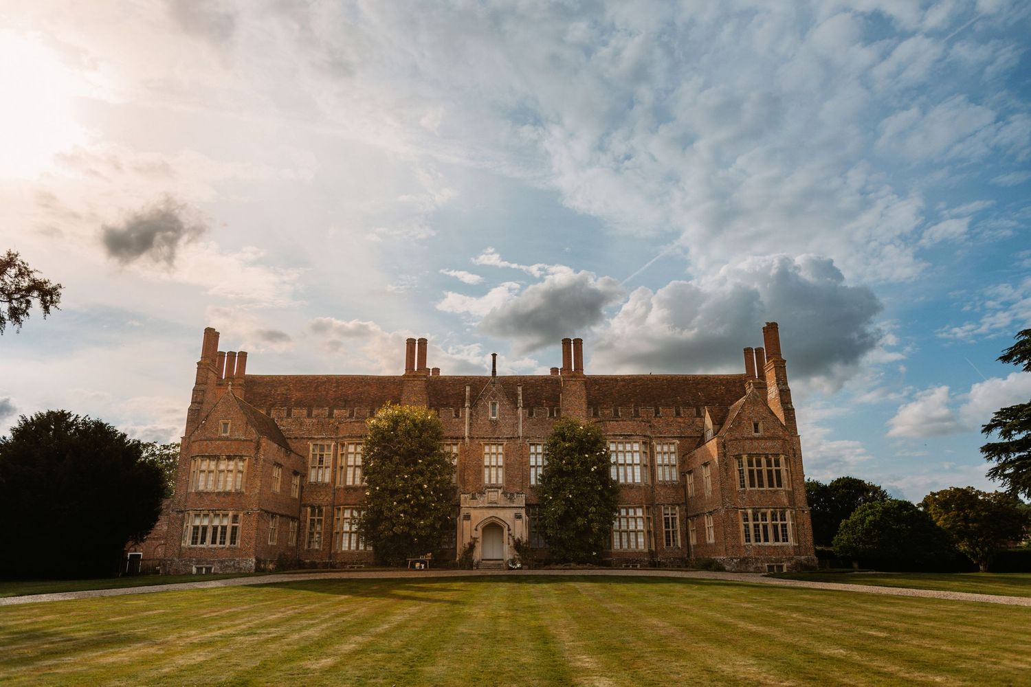 Majestic English manor house with brick facade set against dramatic summer sky.