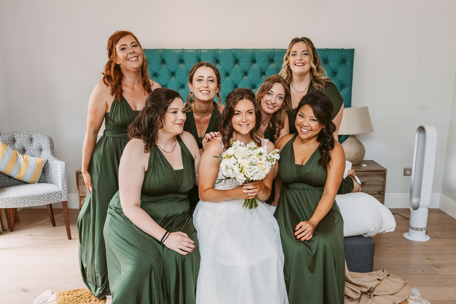 Wedding party in emerald green dresses posing together in elegant room setting.