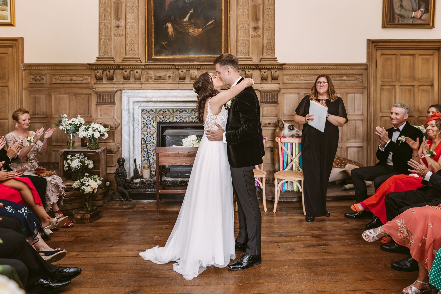 Dancing couple surrounded by seated guests in ornate wood-paneled room with fireplace.