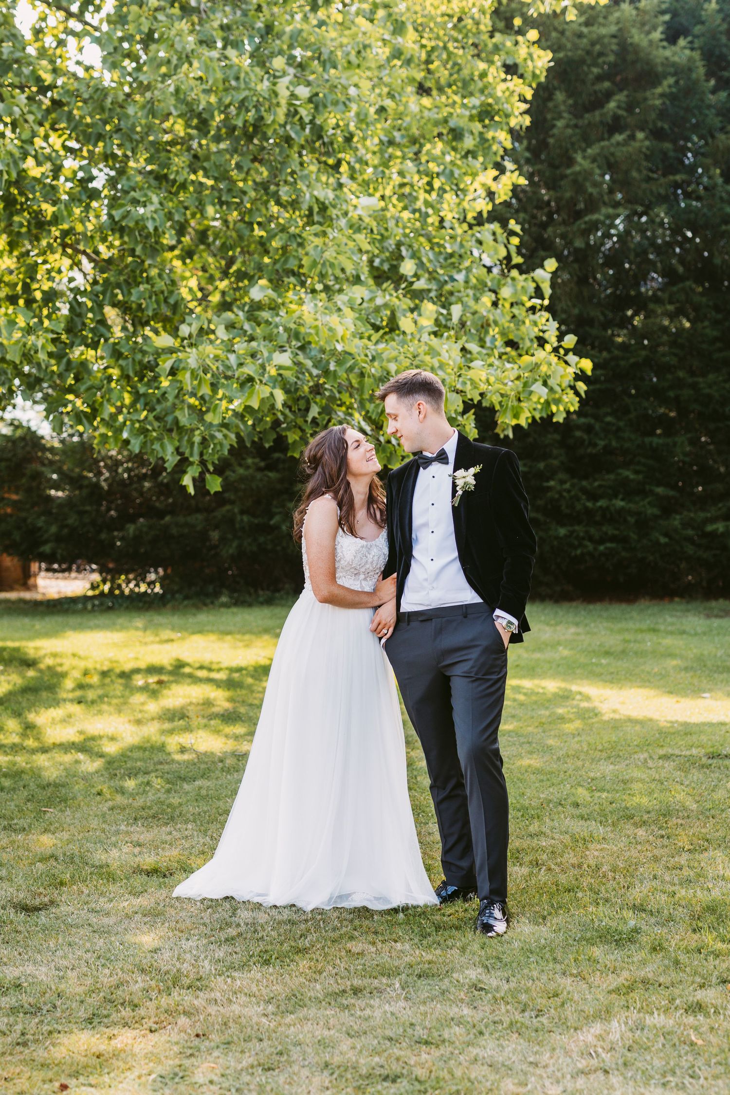 Couple shares romantic moment under green trees on sunny garden lawn.