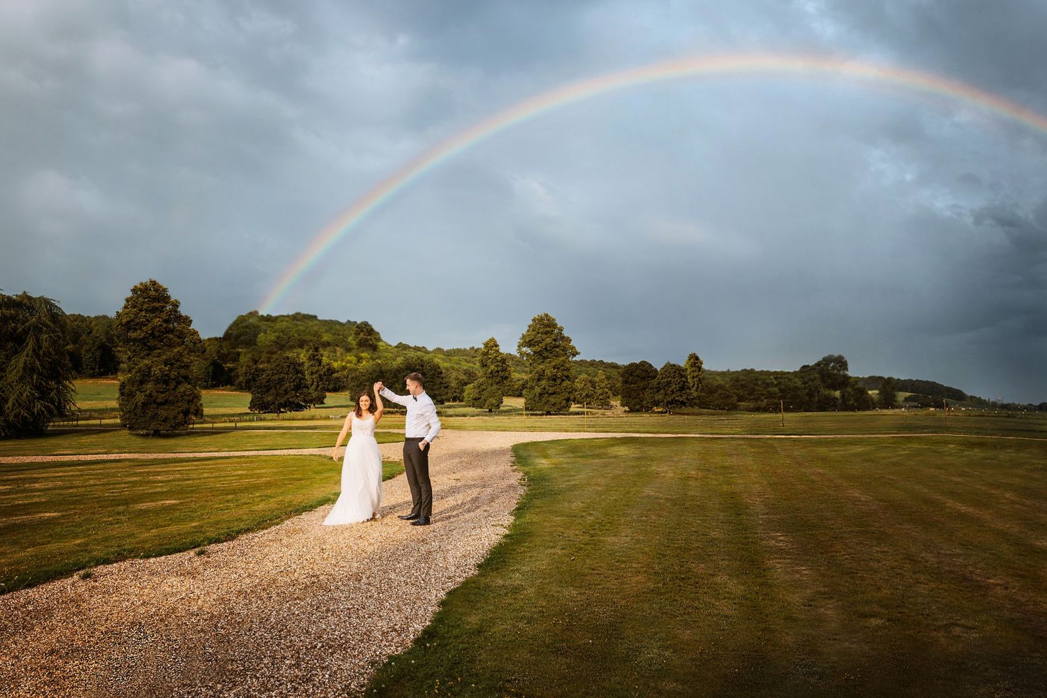 A beautiful rainbow arches over a gravel path on a majestic country estate during a wedding celebration.