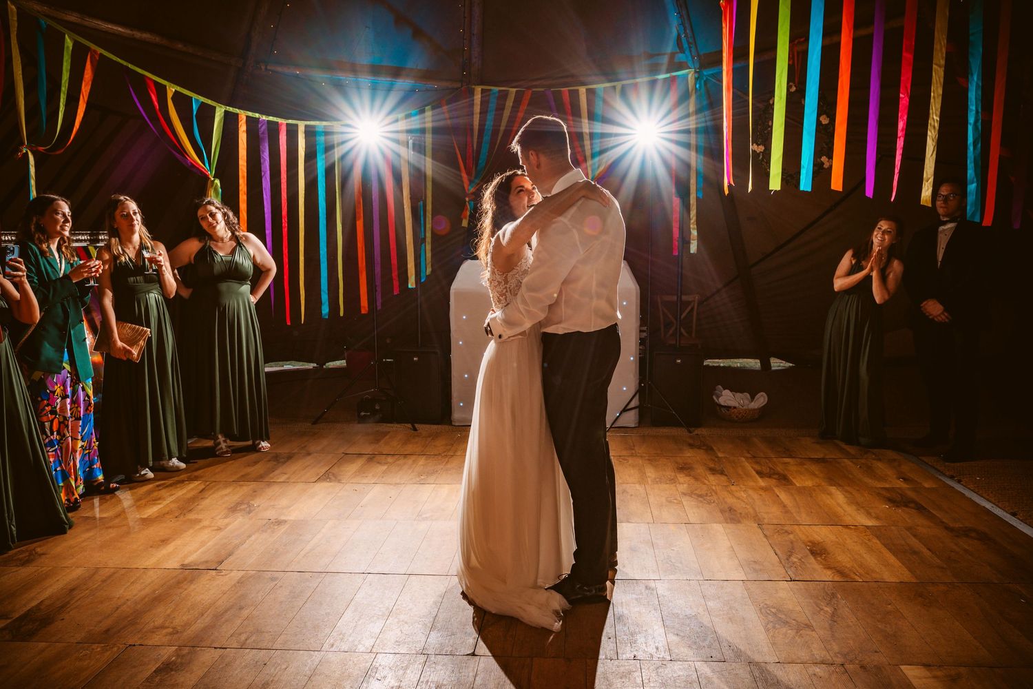 Wedding reception dancers illuminate by colorful lights and streamers in a festive indoor venue.