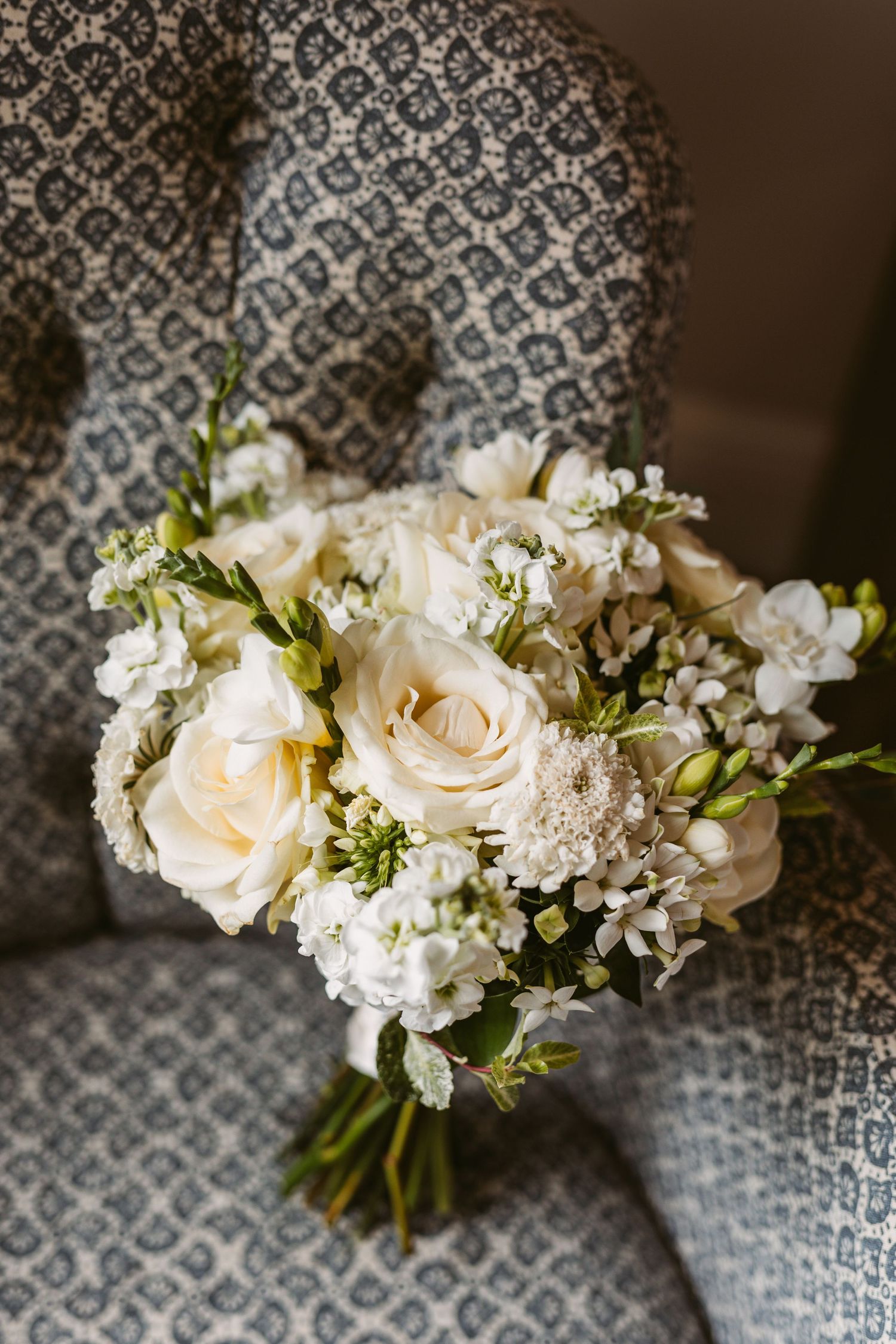 Delicate white rose and hydrangea bridal bouquet resting on patterned upholstery.