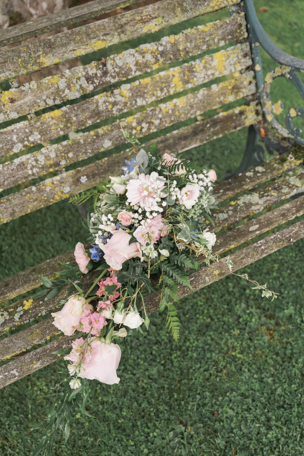 A delicate pink floral arrangement rests on a weathered wooden garden bench.