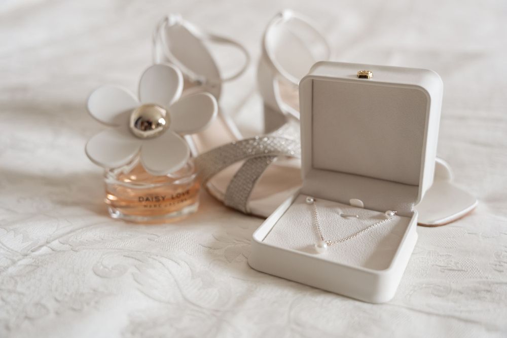 Wedding accessories including a ring box and white floral decorations on white fabric.