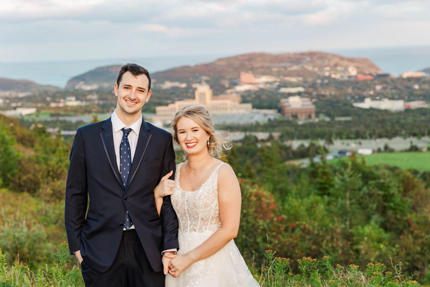 A couple poses in formal attire against a scenic mountain landscape backdrop at their wedding.