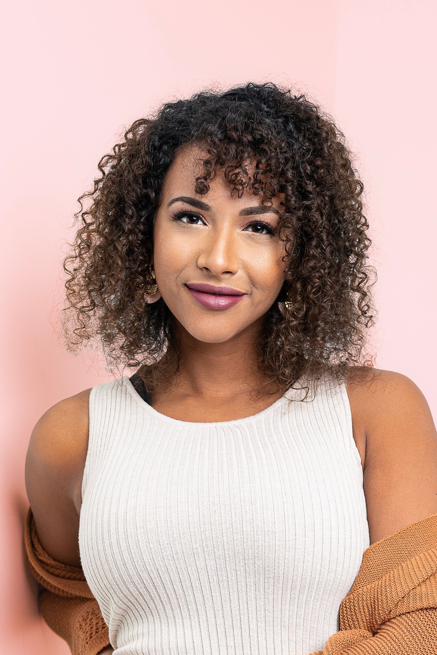 Studio portrait of woman with natural curly hair wearing white top against pink background.