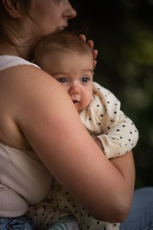 little boy being cuddled by his mum looks over her shoulder into the distance