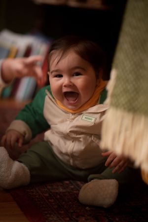 little brown haired boy in cream and green laughs at the camera