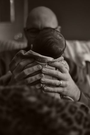 close up of dads hands holding tiny newborn baby while sitting on sofa