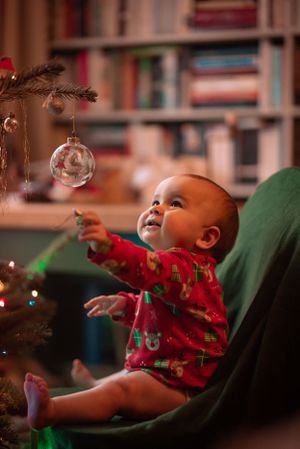 baby is red christmas pyjamas looks up and tries to grab a festive bauble