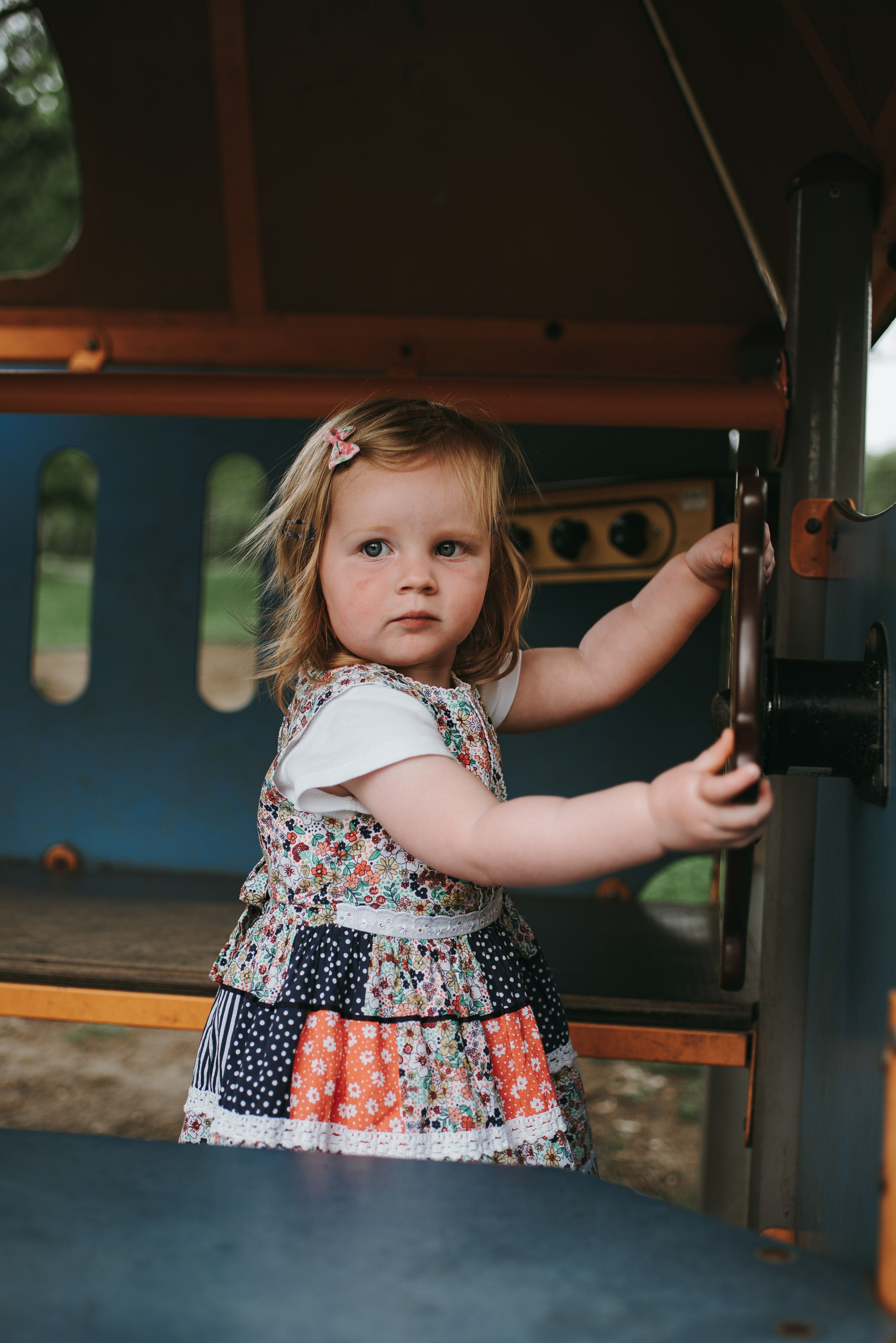 little girl in play park wearing patchwork dress looks at camera with a serious expression