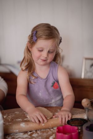 little girl in purple with strawberry blonde hair carefully rolls out cookie dough