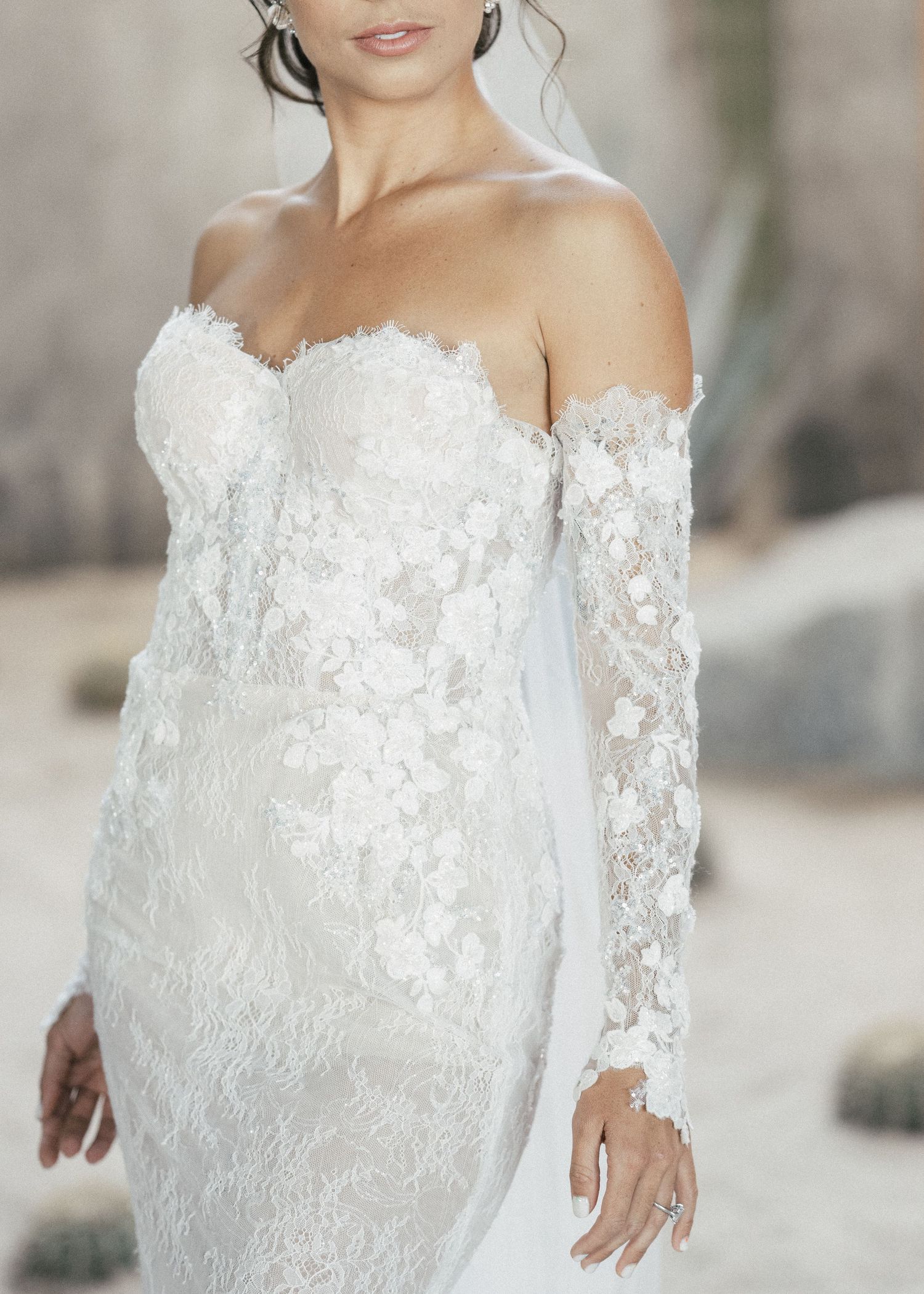 A detailed view of an off-shoulder lace wedding dress with intricate floral patterns.