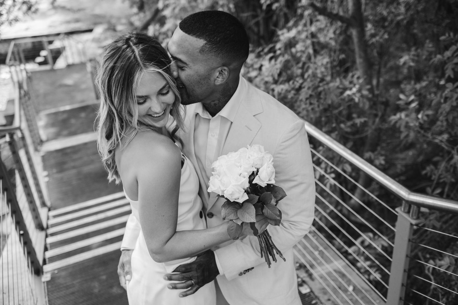A romantic black and white moment on a deck with white outfits and a floral bouquet.