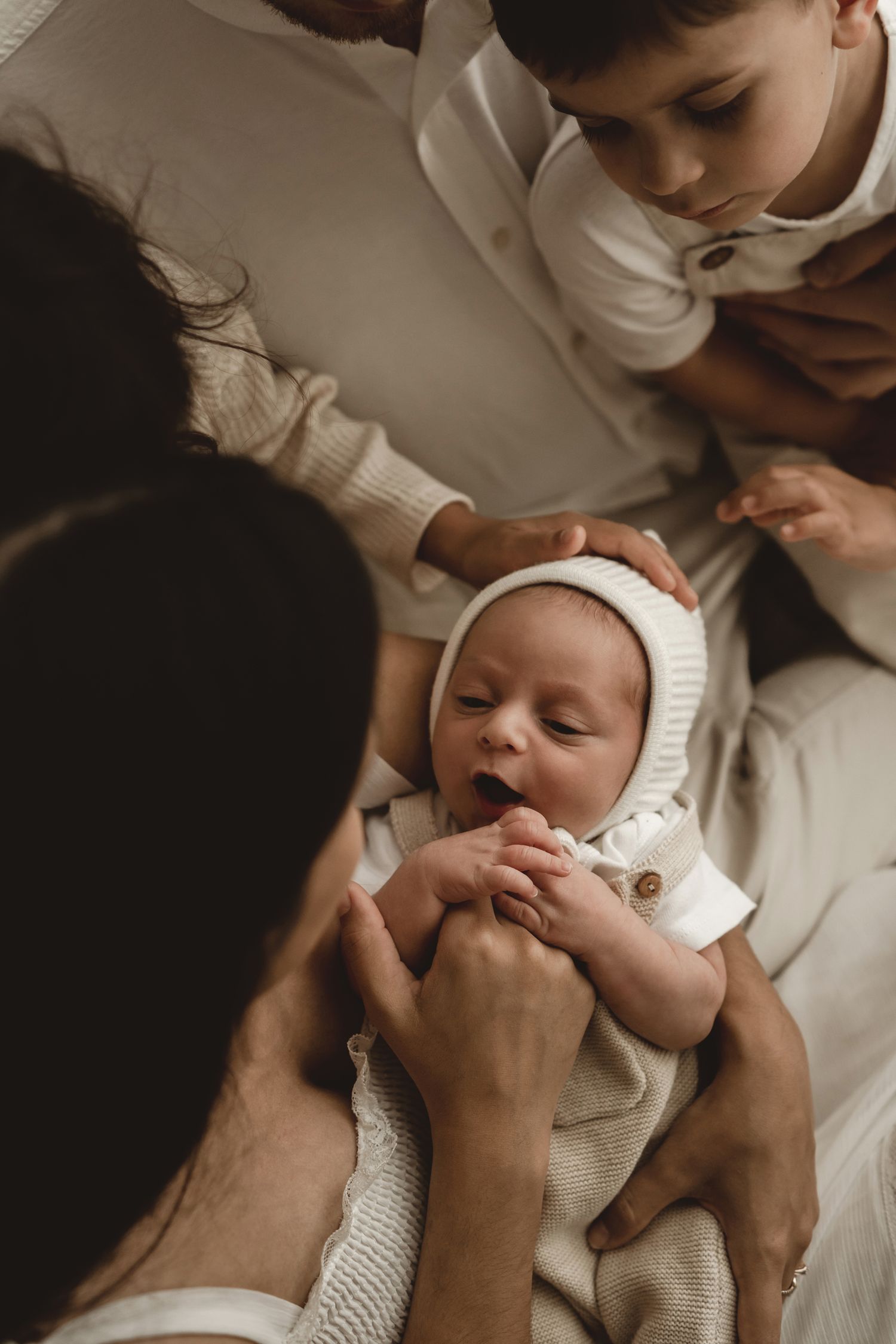 Family members interacting with smiling baby in white bonnet.