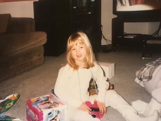 A vintage photo of a child opening presents in a living room setting.