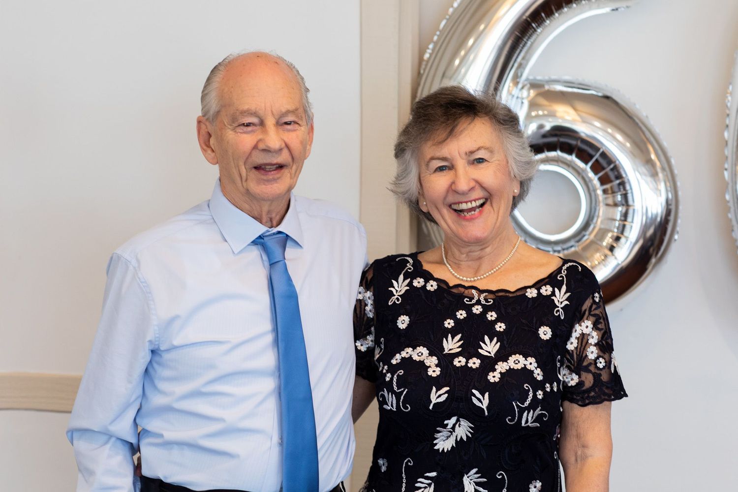 Couple celebrating a 50th anniversary event with silver balloon decorations.