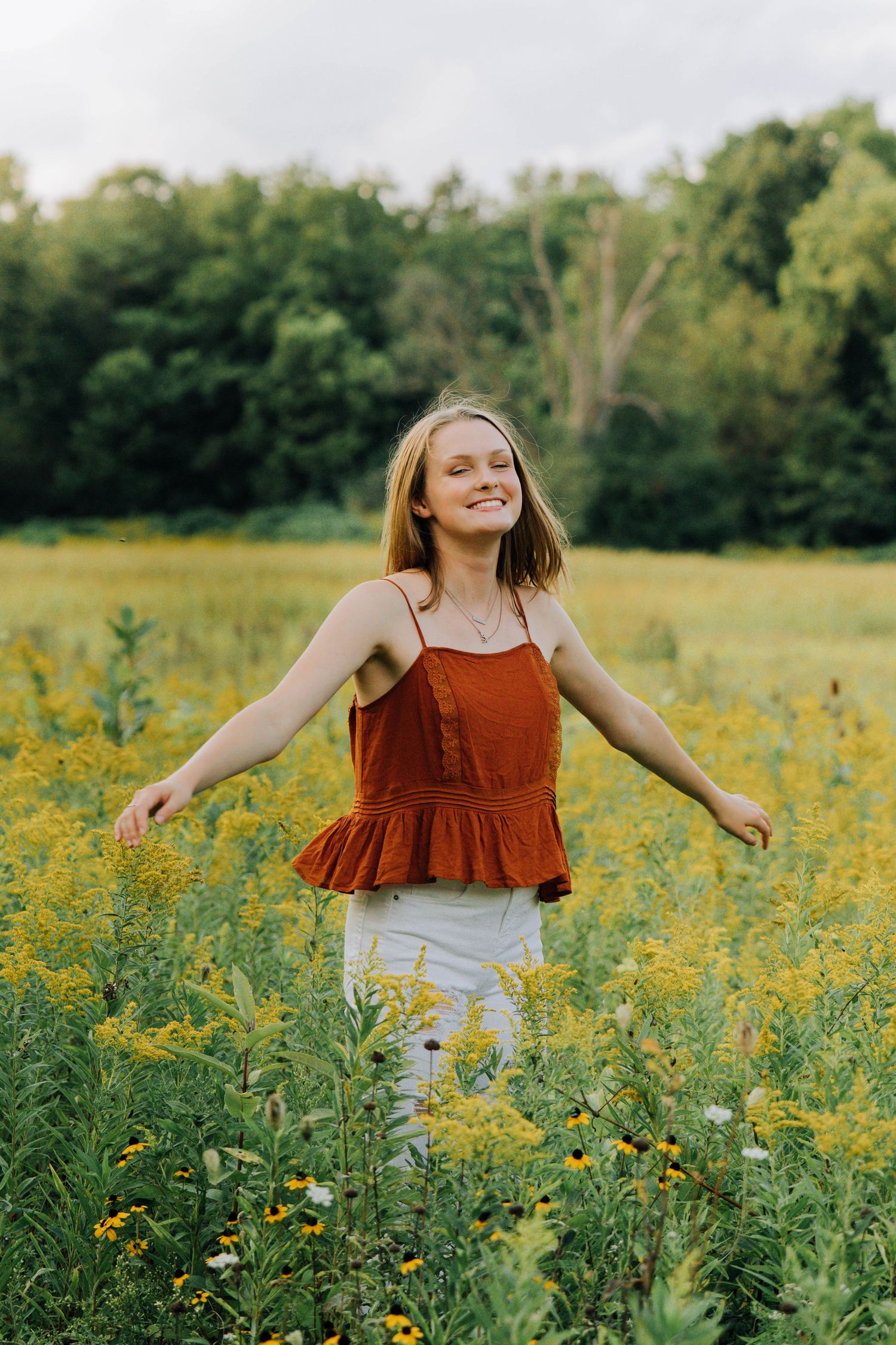 Person walking joyfully through a field of tall yellow wildflowers on a sunny day.
