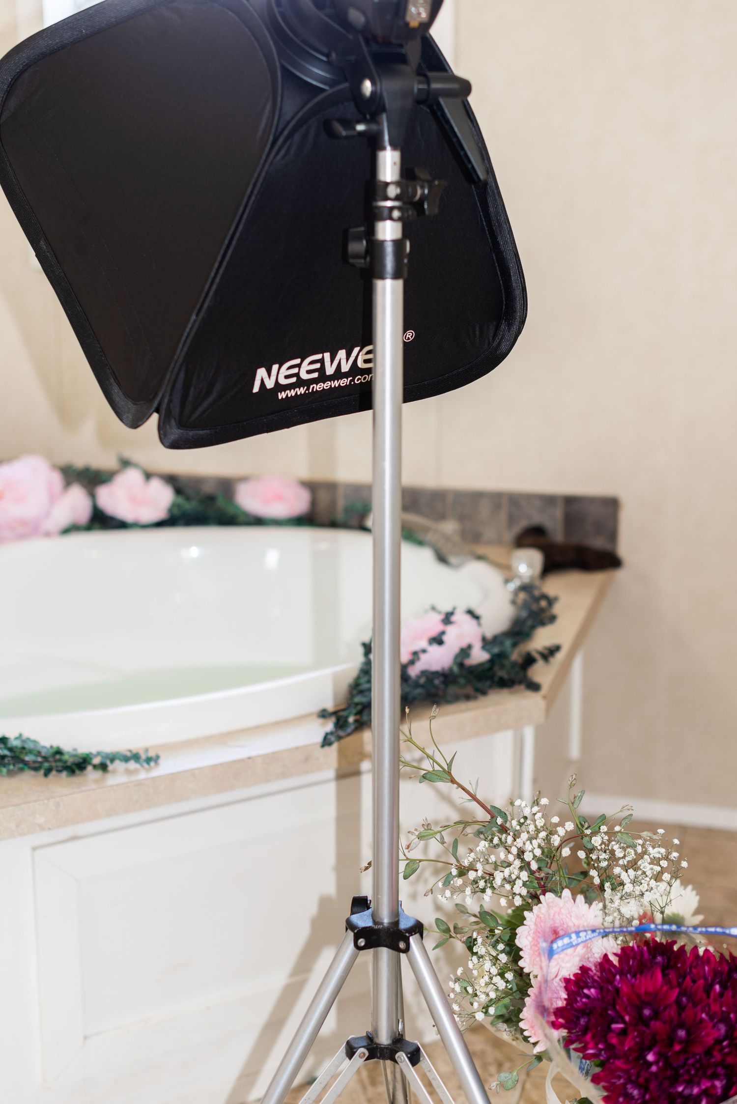 Professional Neewer photography light stand and softbox setup next to floral decorations.