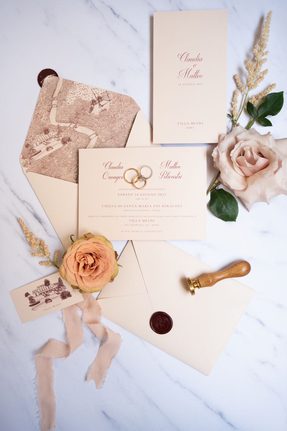 Elegant wedding invitation suite with peach roses and wax seals on white marble background.