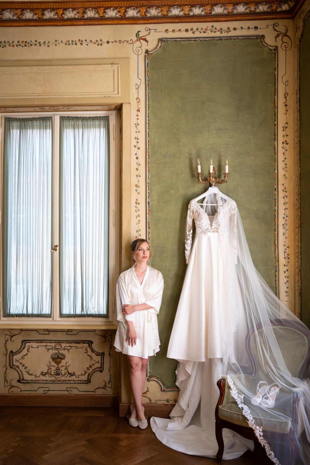 Elegant bridal preparation room with white wedding dress hanging in ornate green room.