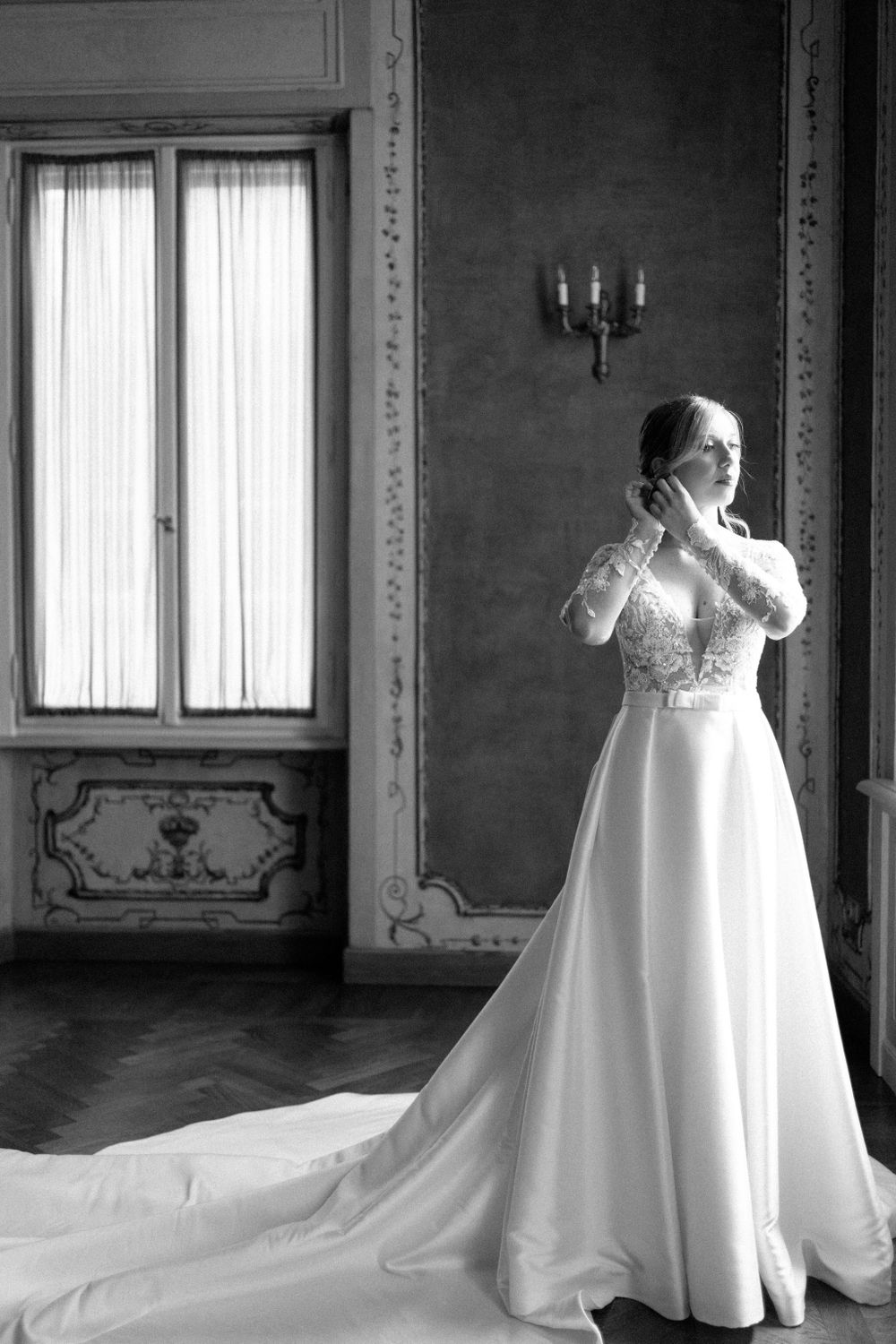 Elegant white wedding dress displayed in a grand room with ornate moldings and natural window light.