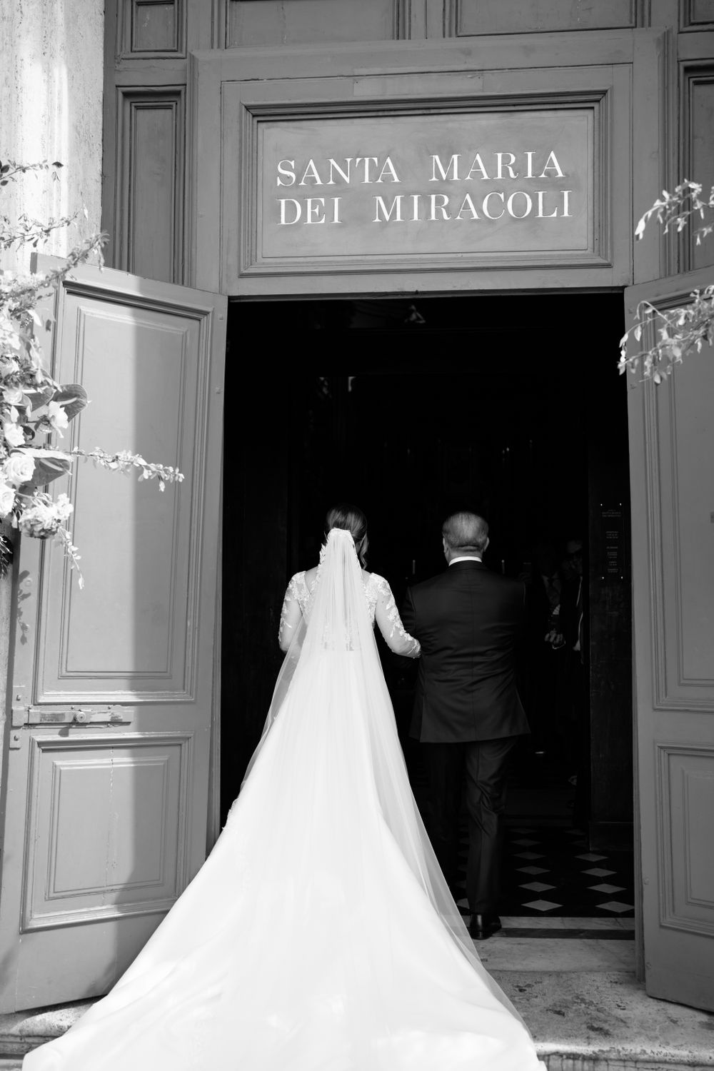 Bride and groom enter Santa Maria dei Miracoli church with dramatic train trailing behind.