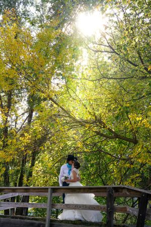 A couple shares an intimate moment on a wooden bridge surrounded by autumn trees.