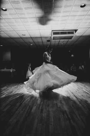 A bride twirls in her wedding dress on a wooden dance floor in dramatic black and white.