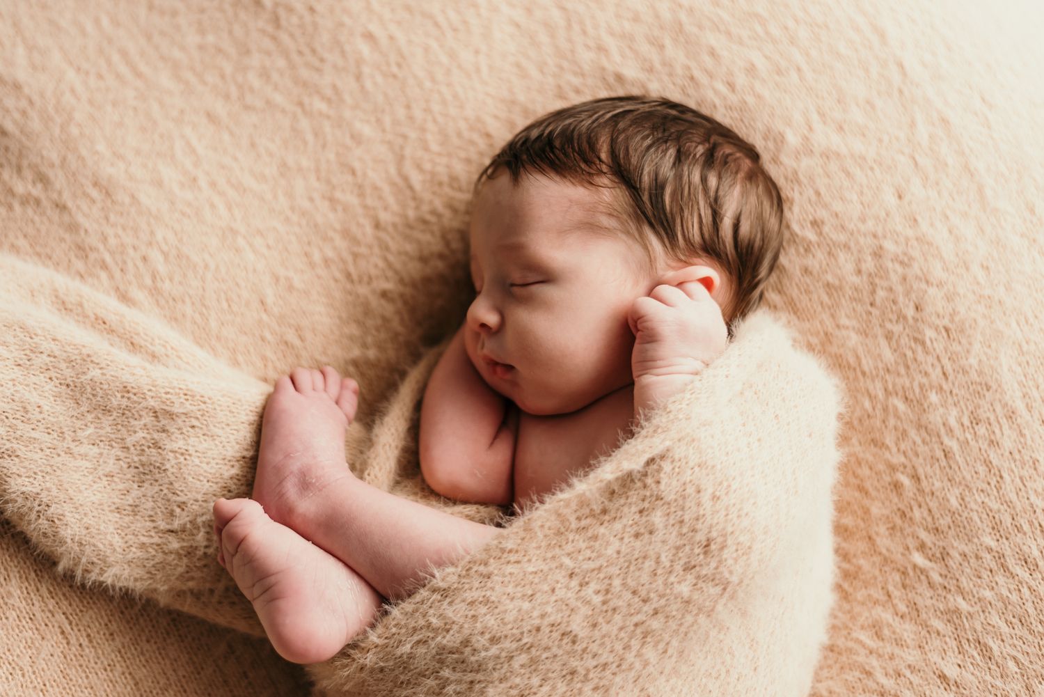 Peaceful sleeping newborn wrapped in warm beige blanket during portrait session.