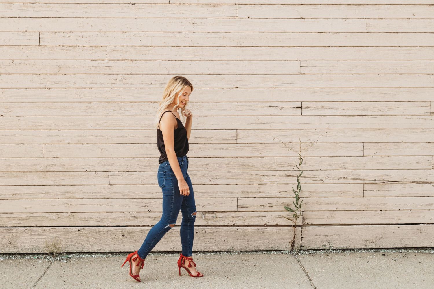 Woman in dark outfit and red heels walking along white brick wall.