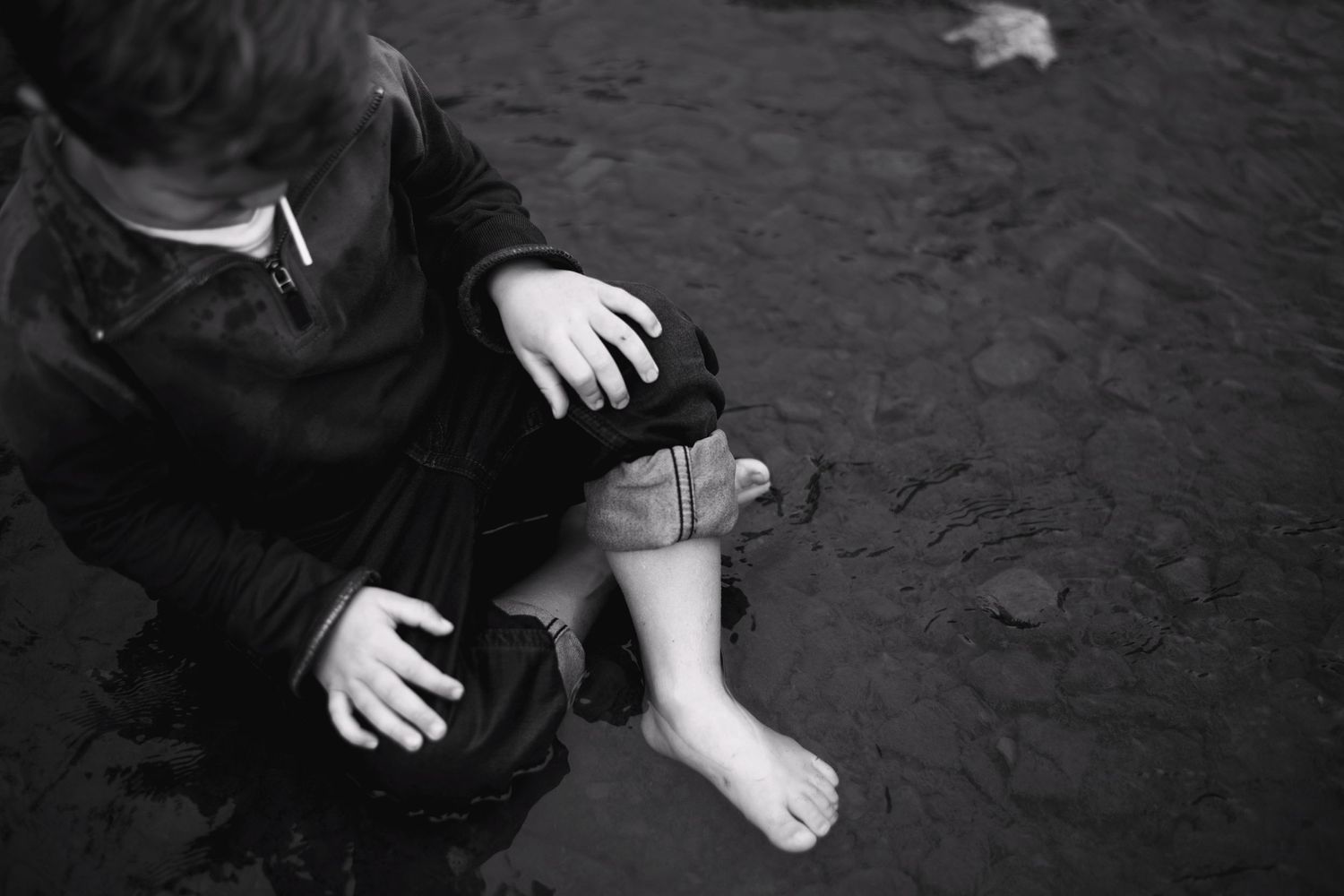 A black and white photo shows small bare feet near hands in dark clothing against a dark ground.
