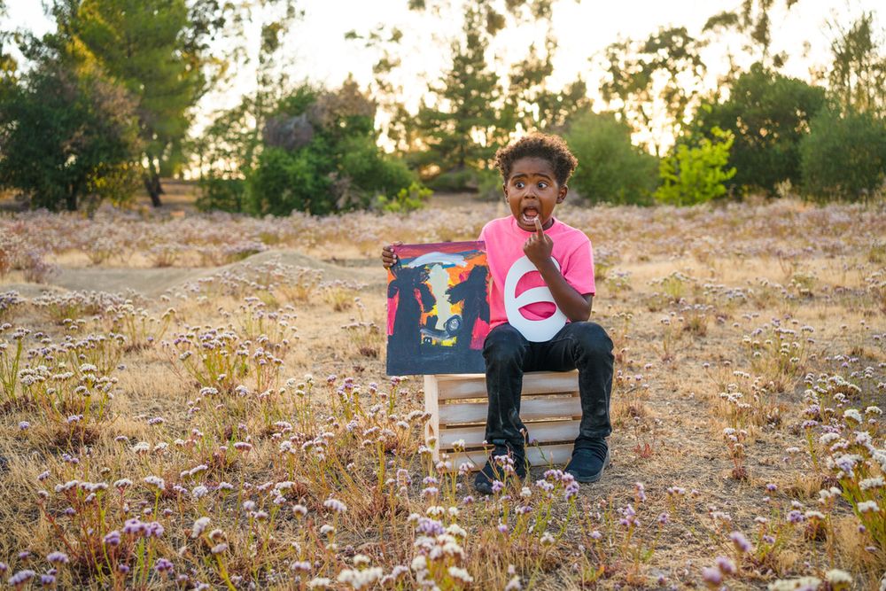 Someone sits in a chair outdoors during sunset holding colorful artwork in a grassy field.