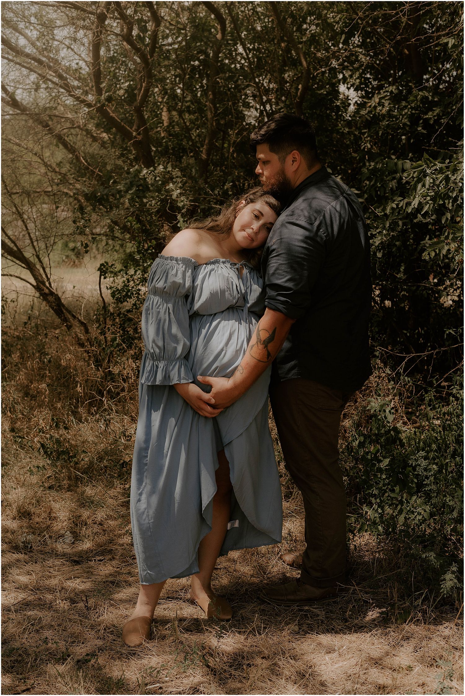 Romantic maternity portrait with couple in natural woodland setting wearing blue dress and dark shirt.