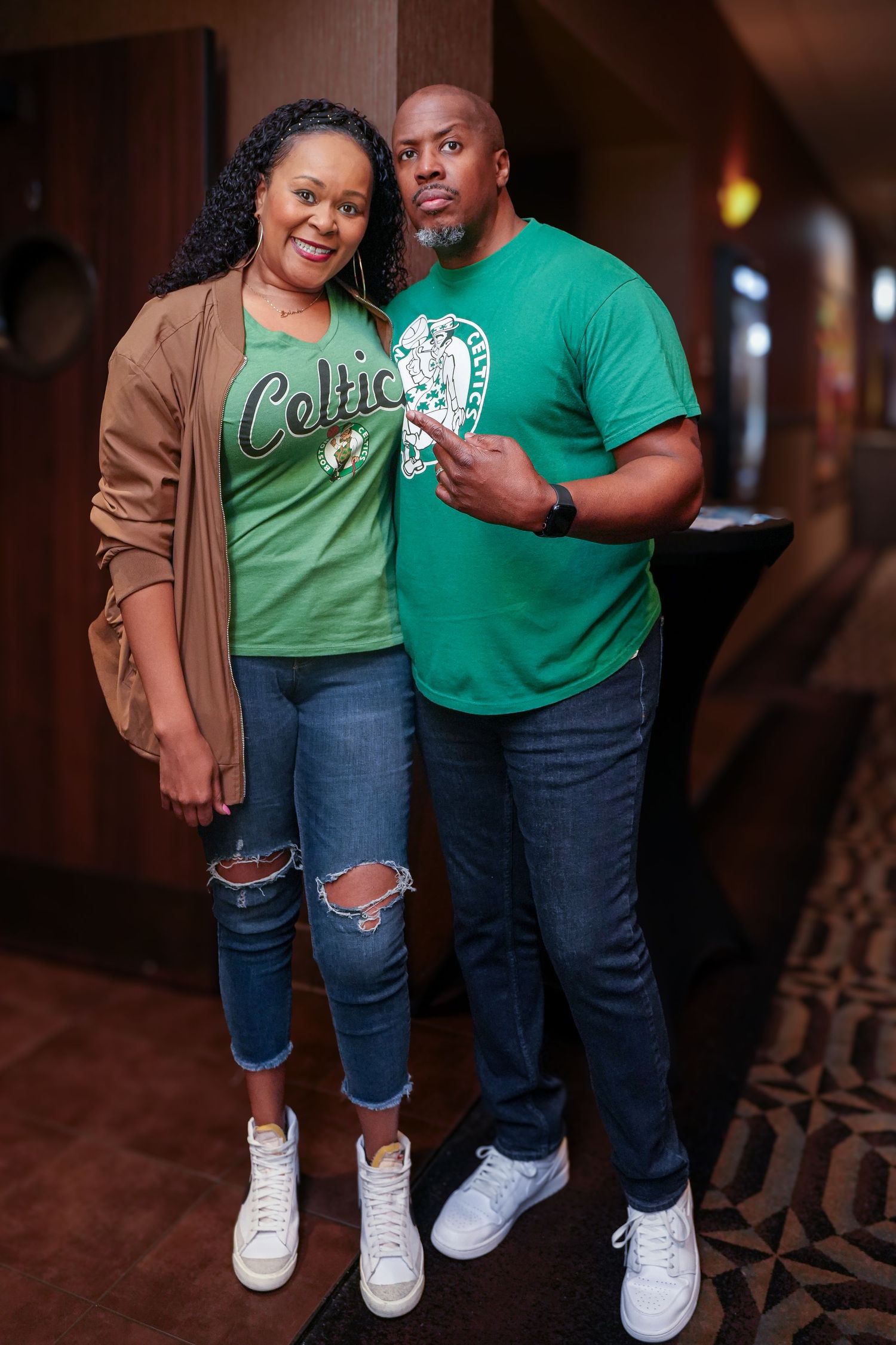 A couple wearing Celtics fan gear poses together indoors.