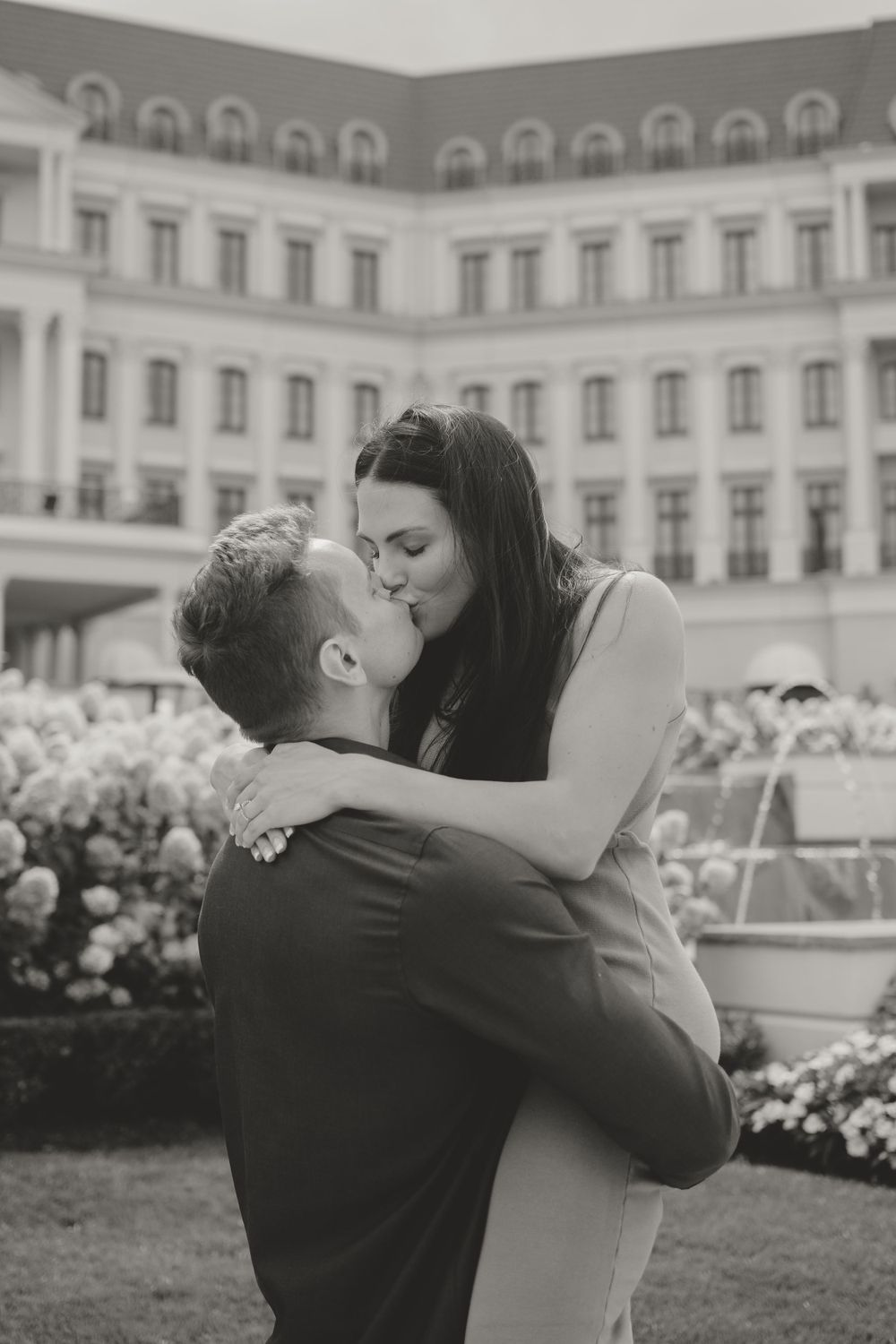 A romantic black and white photo of a couple sharing a kiss in front of a grand building.