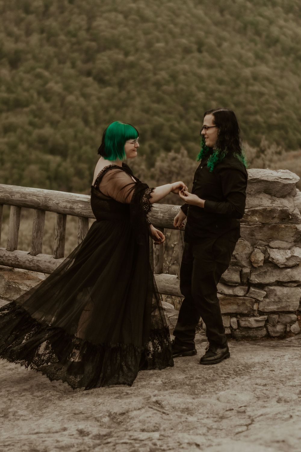 Couple dancing together on a stone wall in a dramatic black dress and casual outfit.