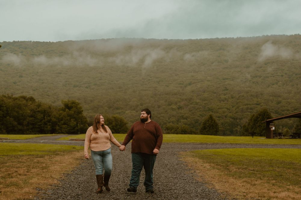 A couple walks hand in hand through a scenic mountain landscape at sunset.