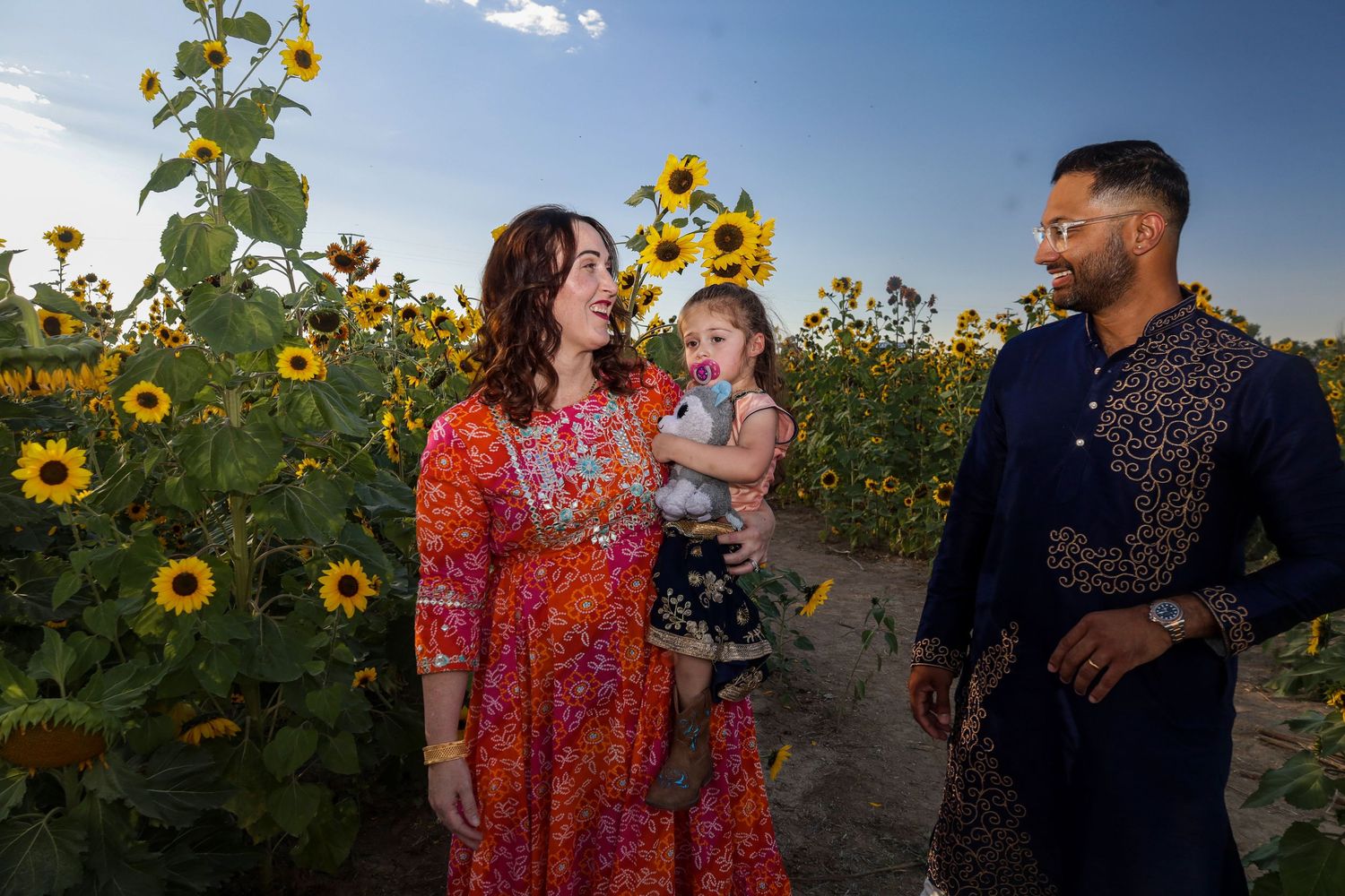 Family in colorful attire posing in sunflower field during golden hour.