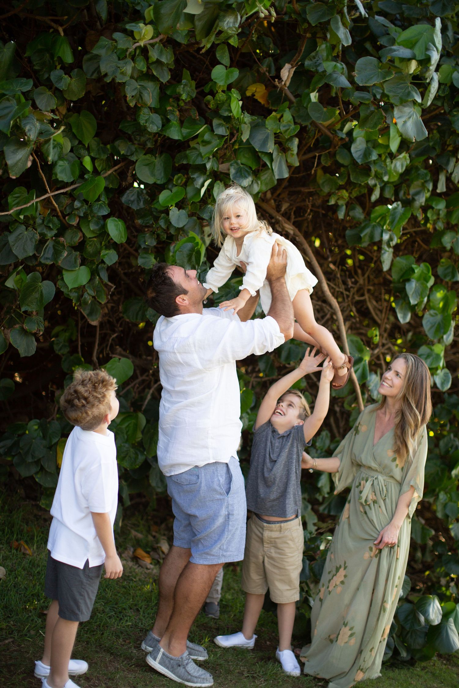 Family playing together outdoors against lush green foliage background.