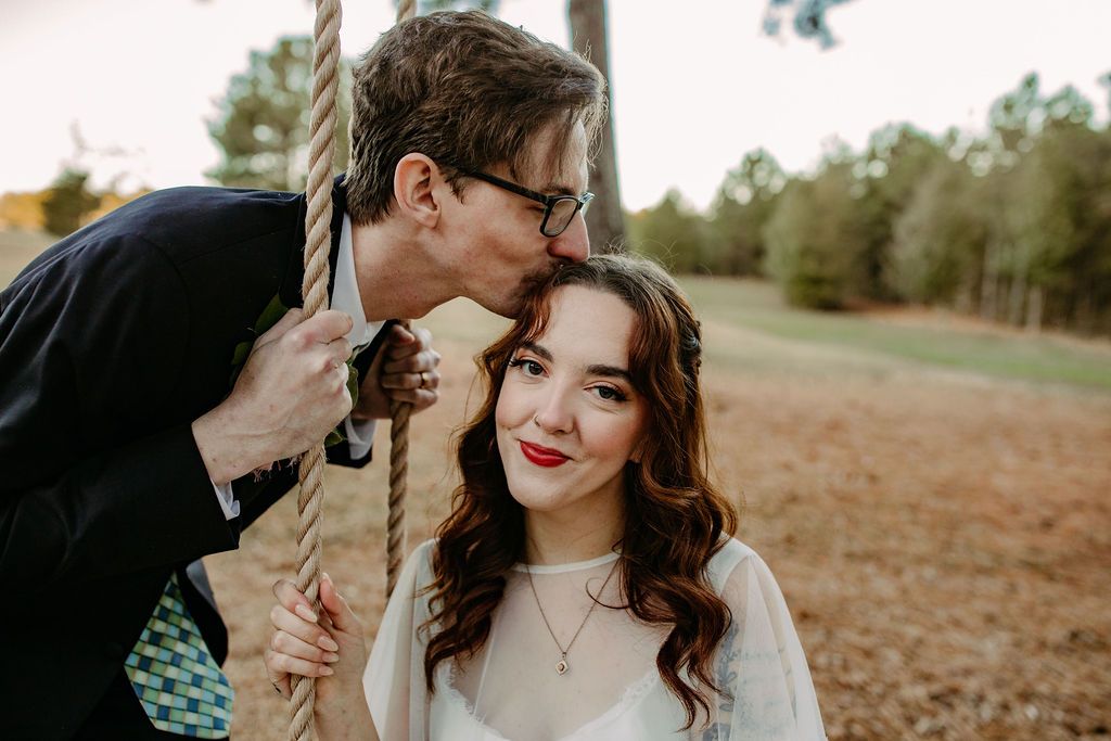 Bride and groom pictures in open field on swing under tree at Sanctuaire Atelier.