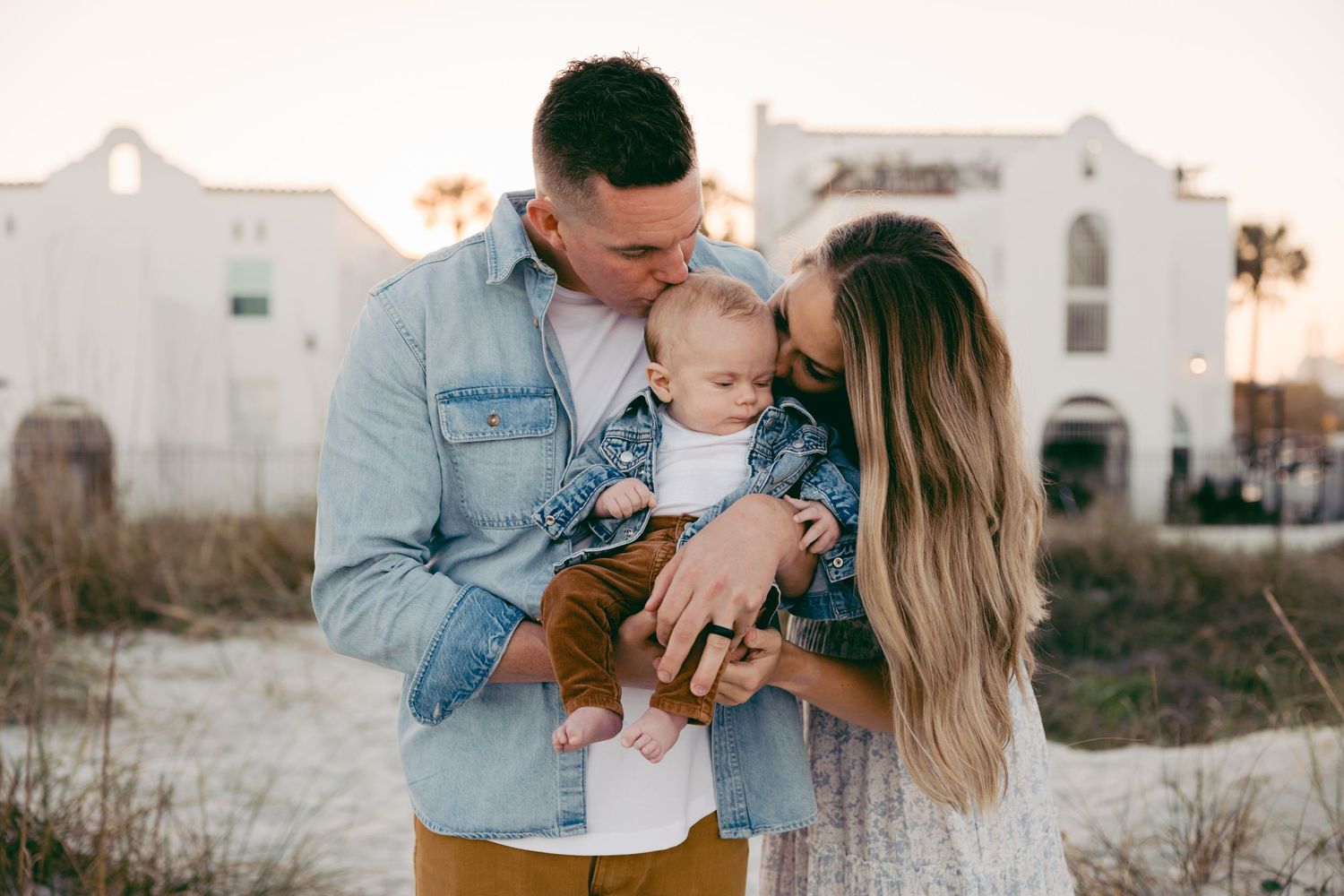 Family of three kissing their son on the head on the beach