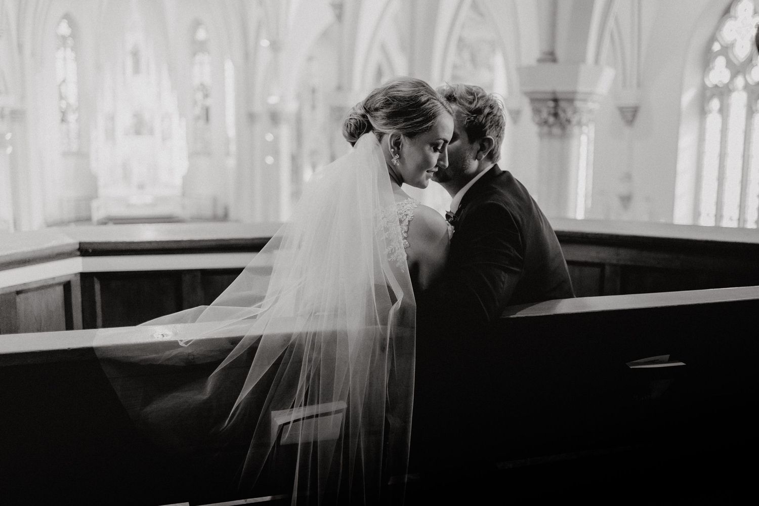Groom whispering in bride's ear in church pew.