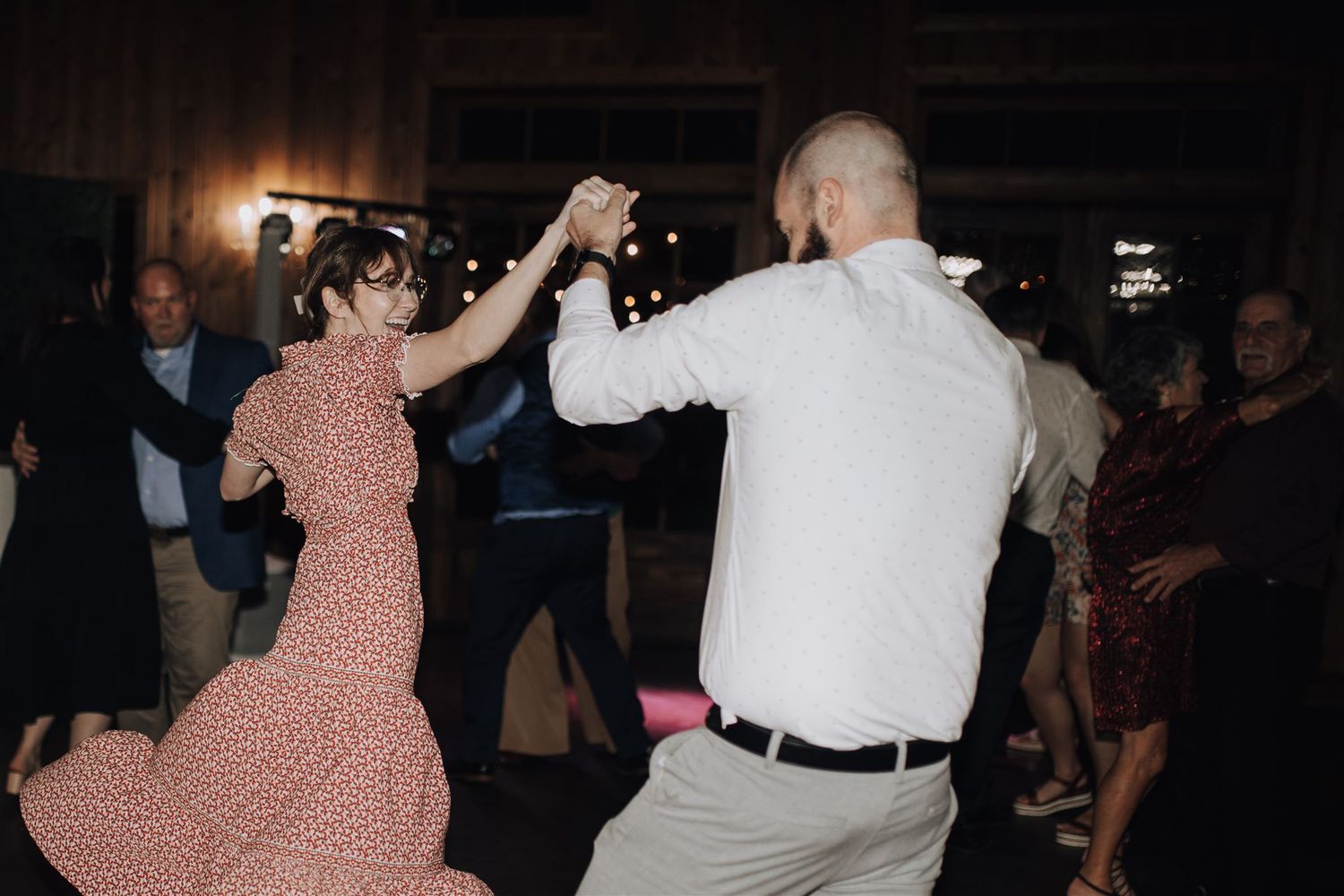 Wedding guests dancing energetically in a dimly lit venue with polka dot dress and white shirt.