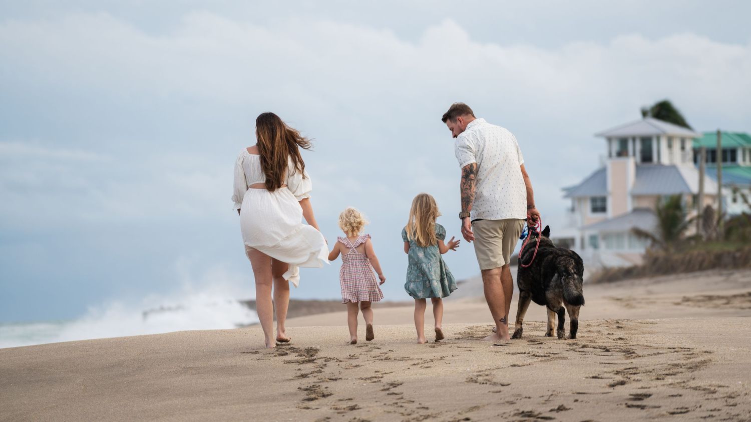 Family walking on beach with their dog as waves crash near coastal homes.