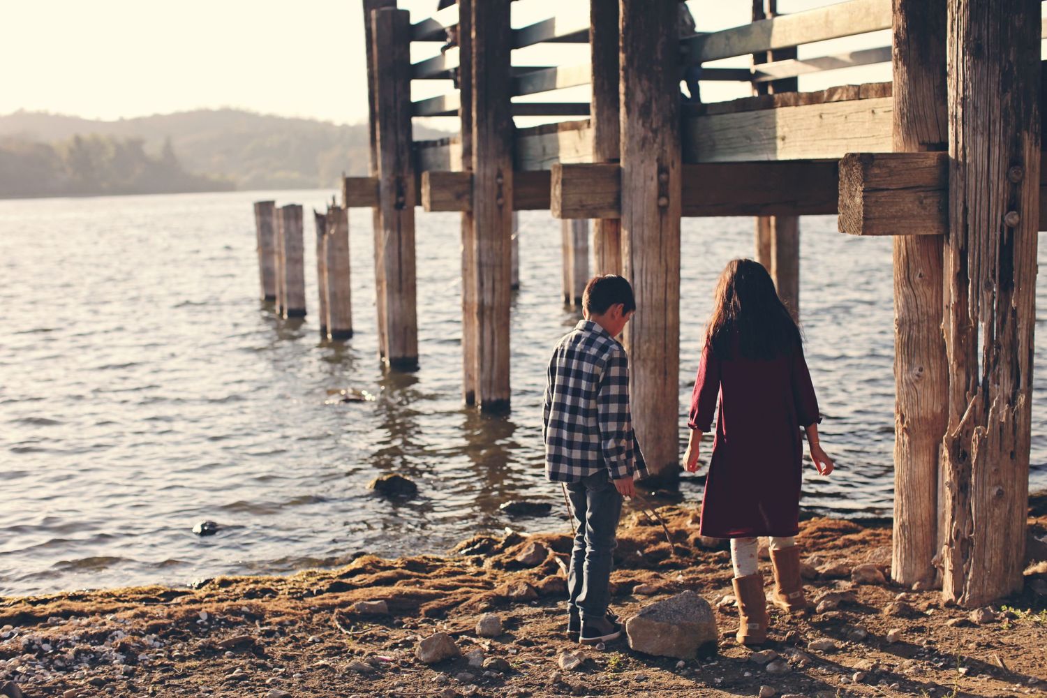 Two people walking along a wooden pier at sunset near a lake.