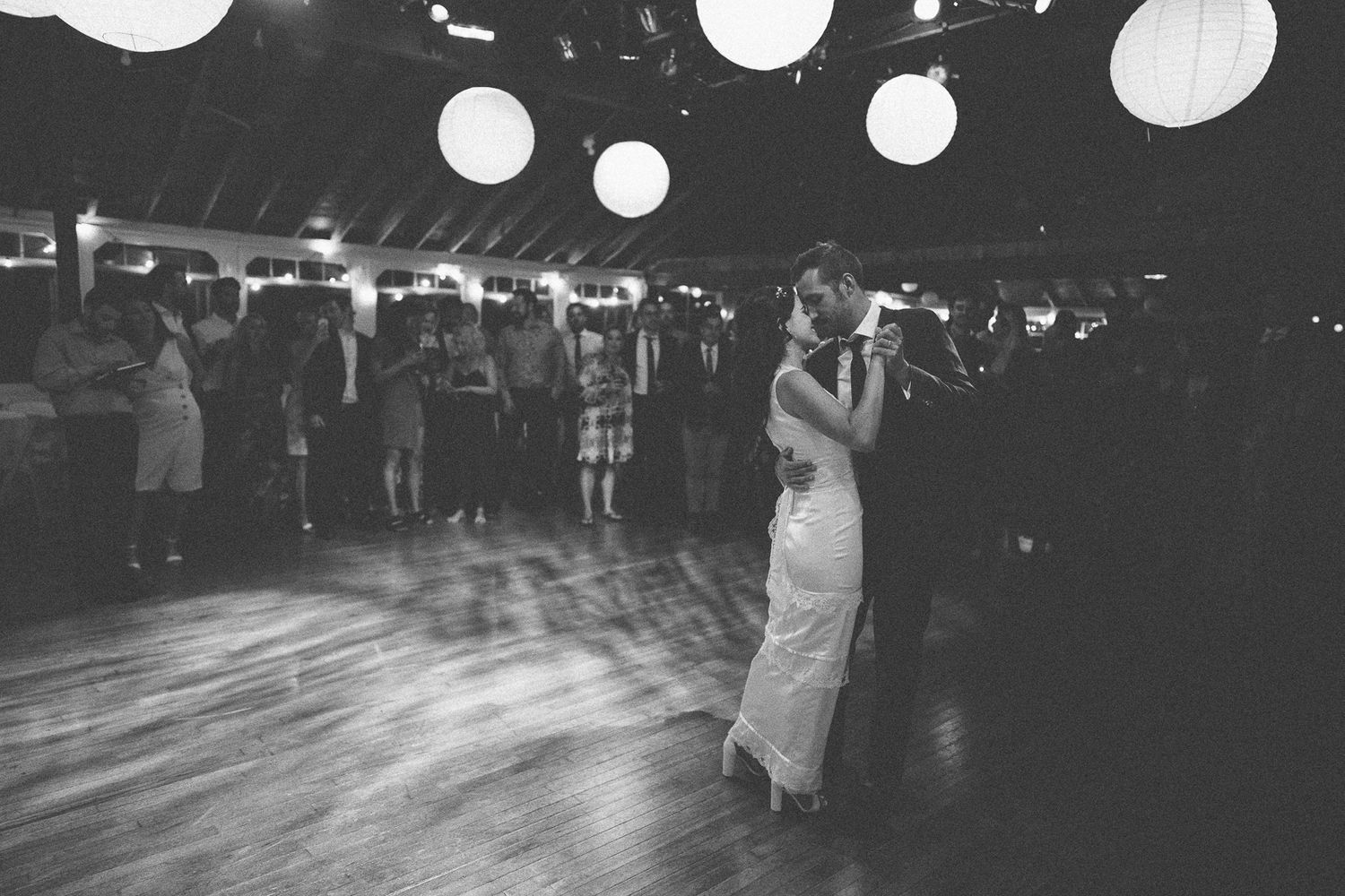 Black and white photo of a couple dancing under paper lanterns at a wedding reception.