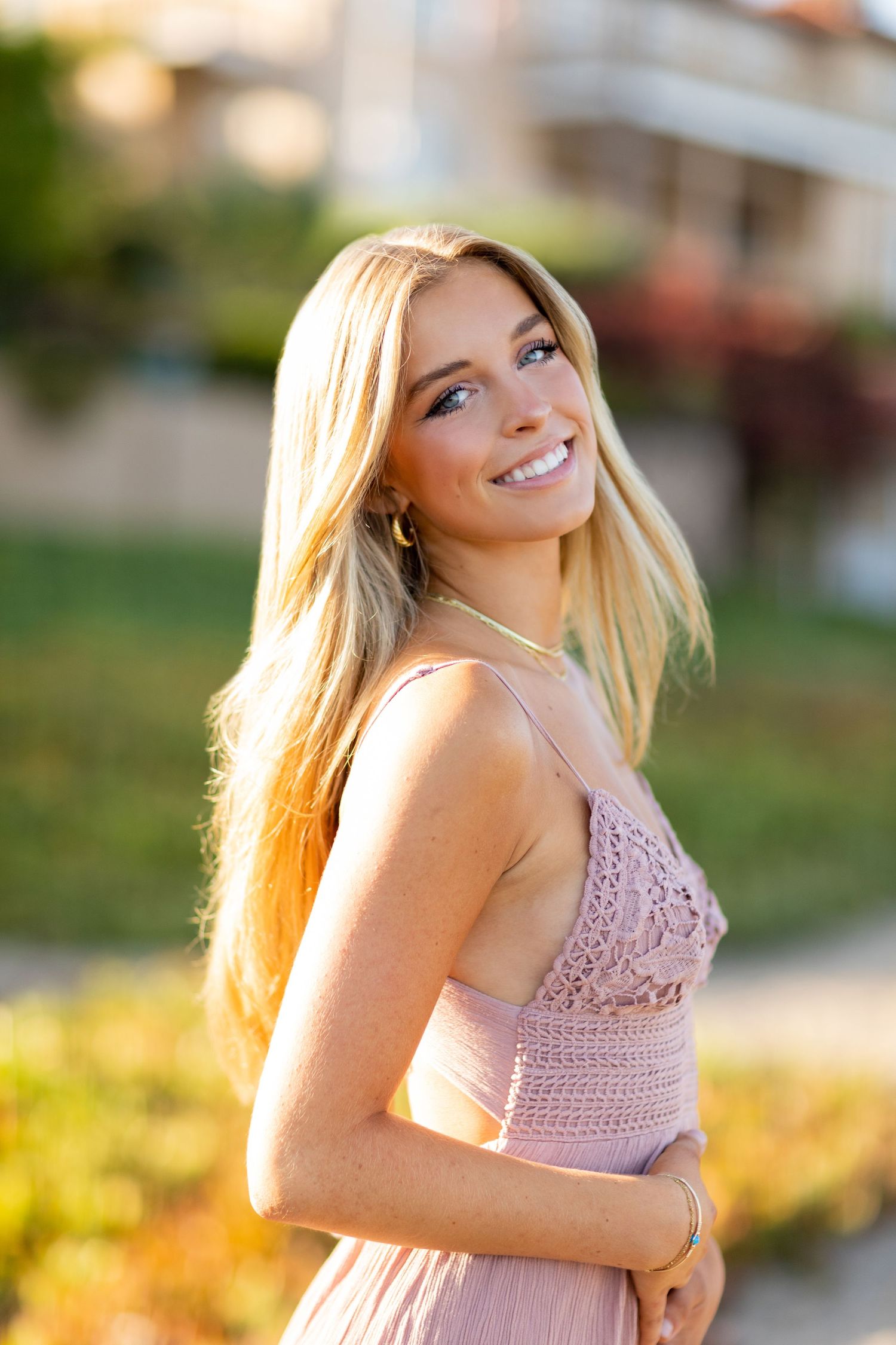 A high school senior in pink lace dress during golden hour outdoor photoshoot.