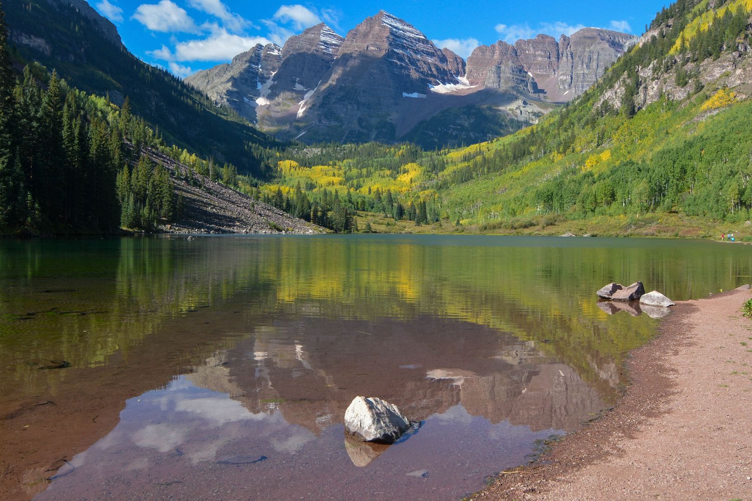 Scenic Maroon Bells peaks reflect in crystal clear alpine lake surrounded by Colorado wilderness and autumn colors.